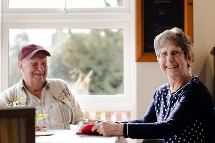 Two care home residents sat smiling at a table taking part in care home activities